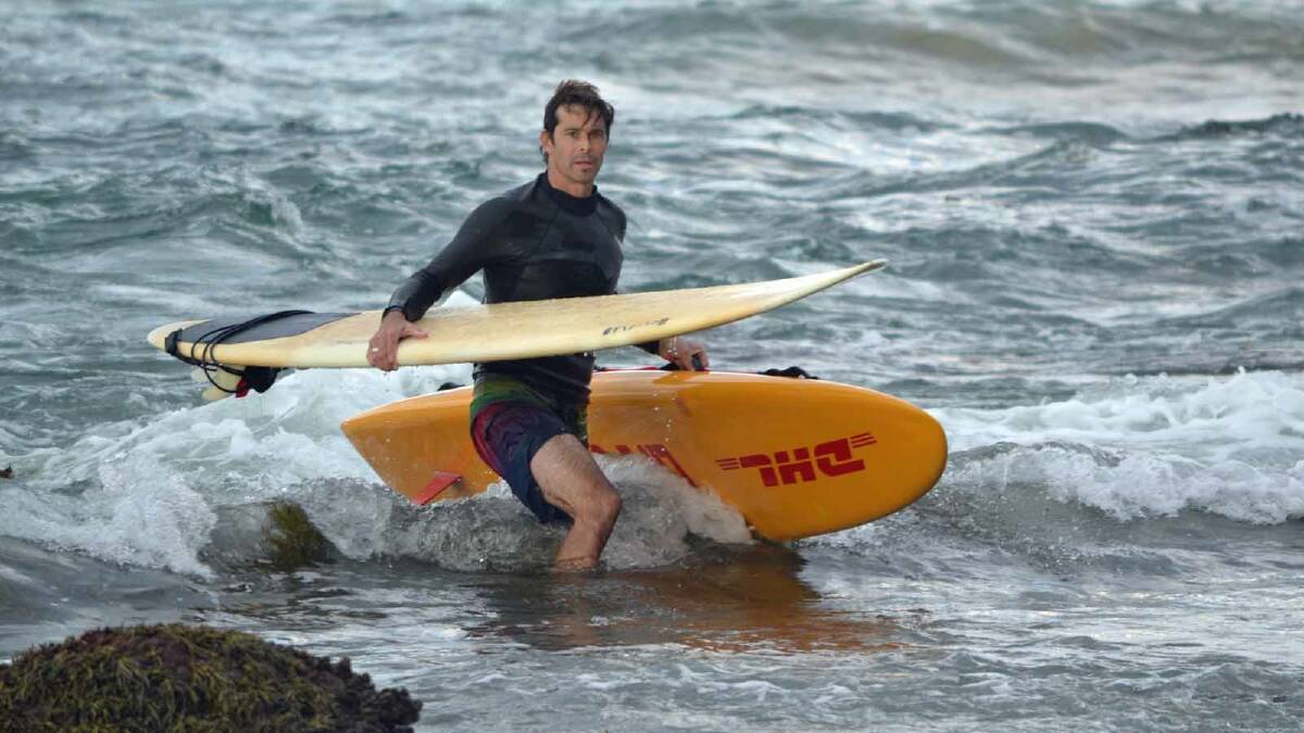 RESCUE: Lifeguard Adrian Wright returns to shore with a surfboard belonging to the people washed onto rocks.
