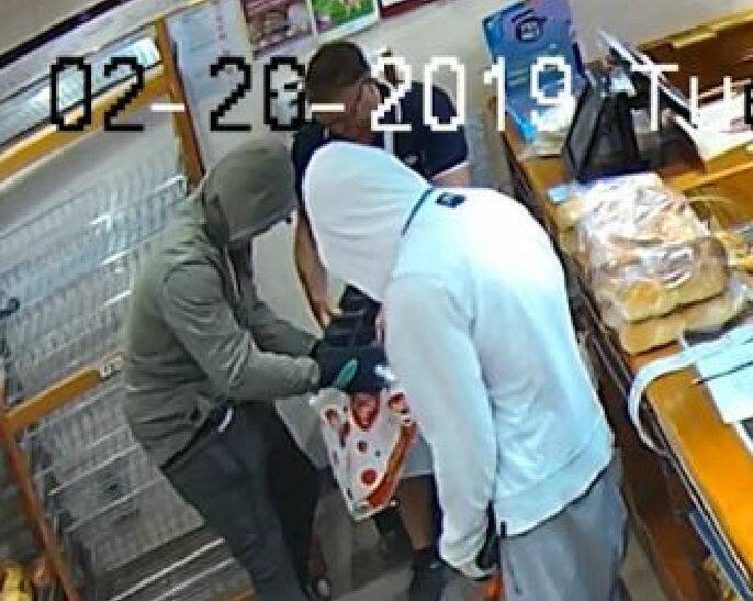 Two alleged offenders with a staff member emptying contents of the cash register into a plastic bag.
