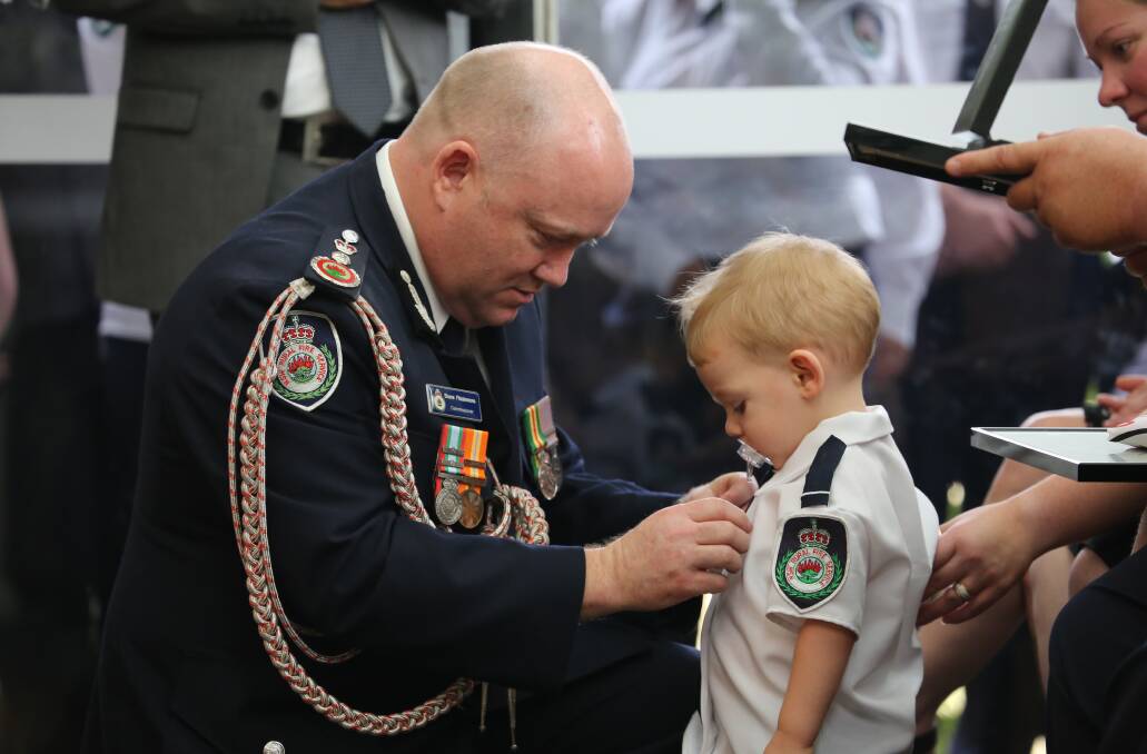 SPECIAL: James Morris' stunning photo of then NSW RFS Commissioner Shane Fitzsimmons pinning a Commissioners Commendation Medal onto 19-month-old Harvey Keaton, at his father Geoffs funeral.
