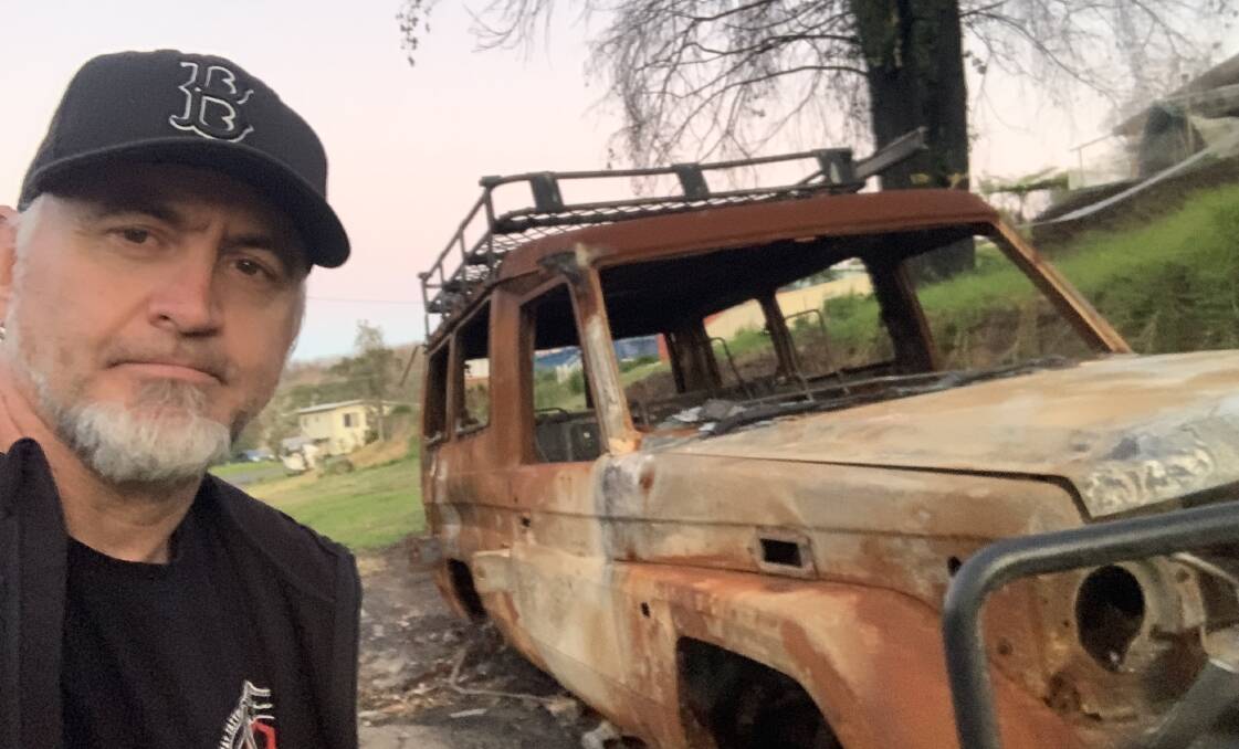 TOLL: Anthony 'Ash' Brennan with a burnt-out vehicle at Conjola.