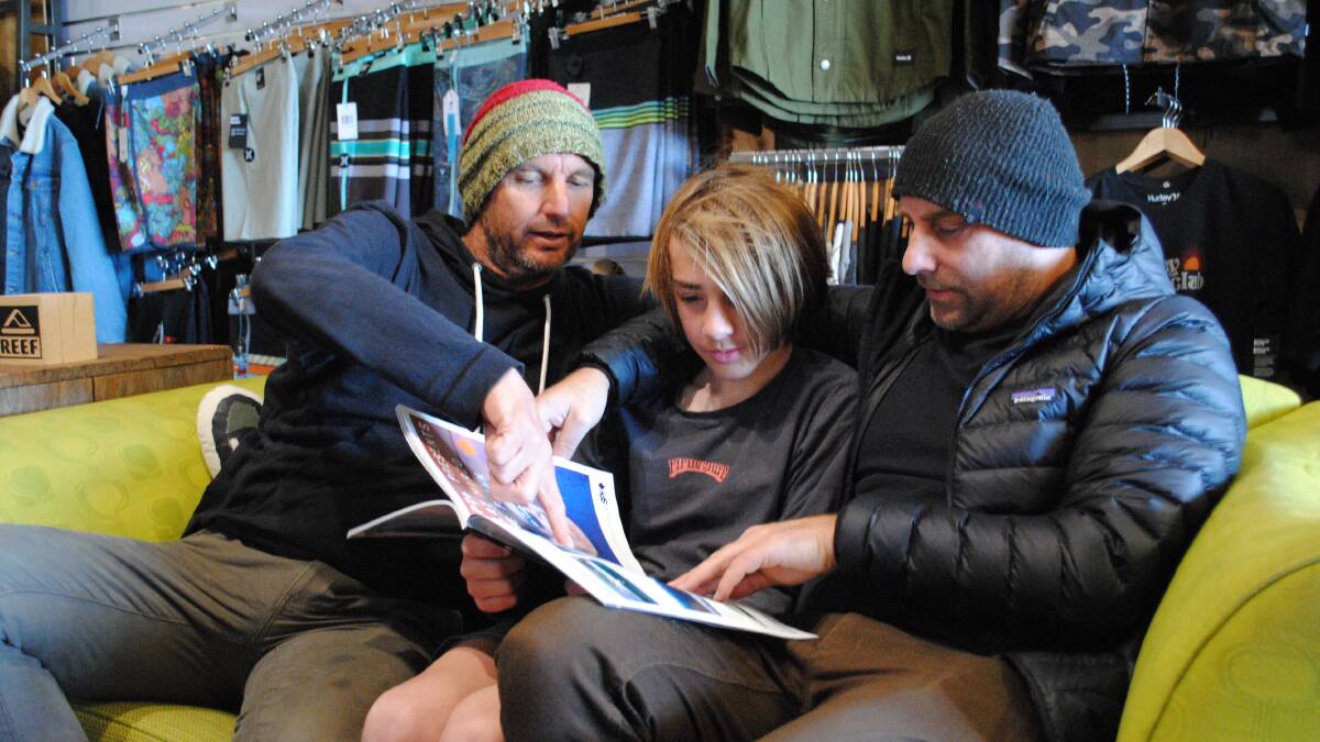MATESHIP: Surfers Unite to Fight Suicide organisers Garth Dickenson and Kurt Nyholm flip through the pages of a surfing magazine with Kurt's son Seth (centre).