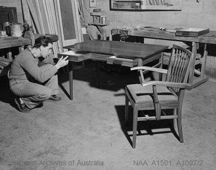 Oswald Paseka puts the finishing touches on a writing table he made for the library of the Legislative Council Chamber in Kuala Lumpur. Image courtesy of the National Archives of Australia.
